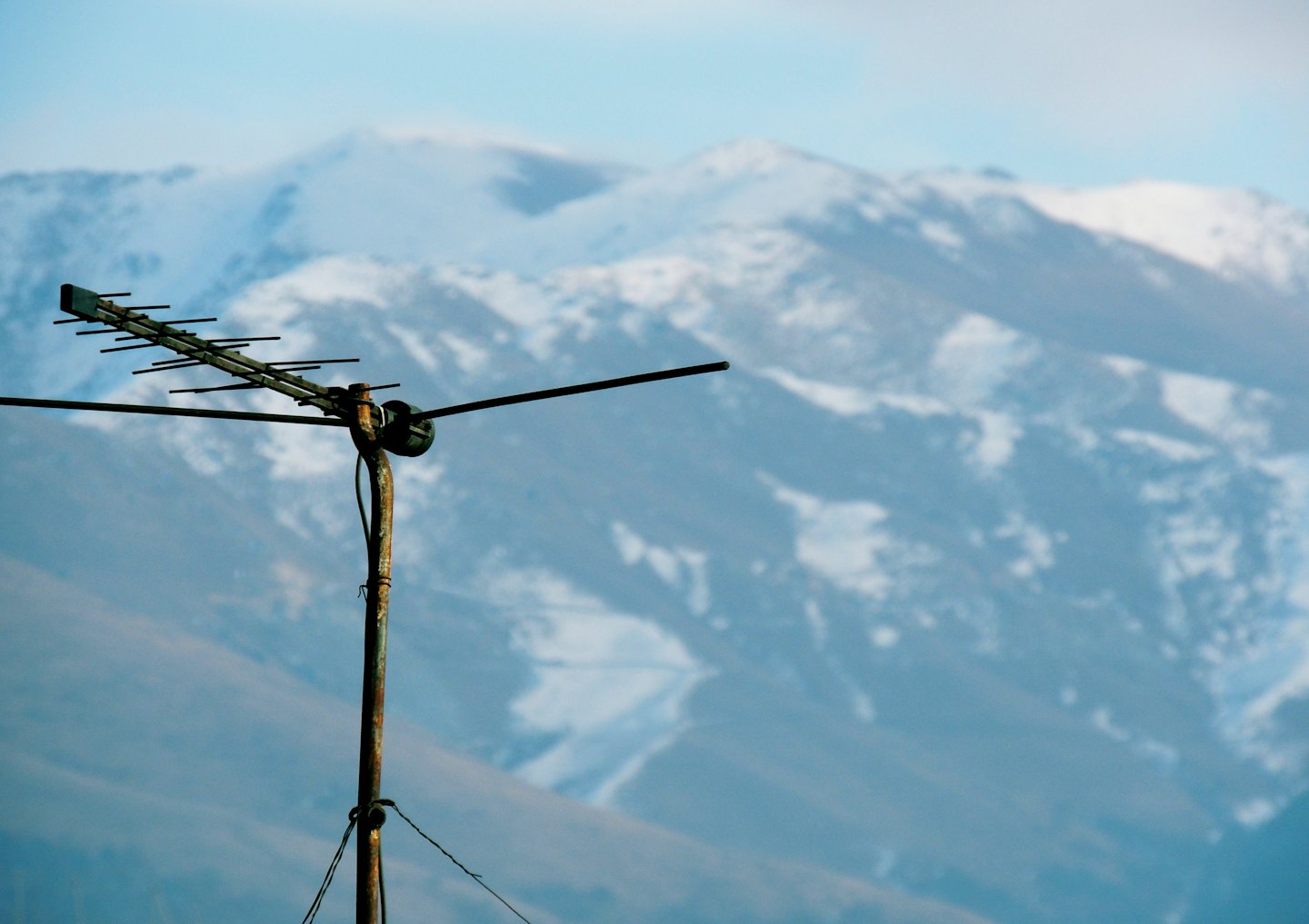 Rusty television antenna standing before snow-capped mountains.
