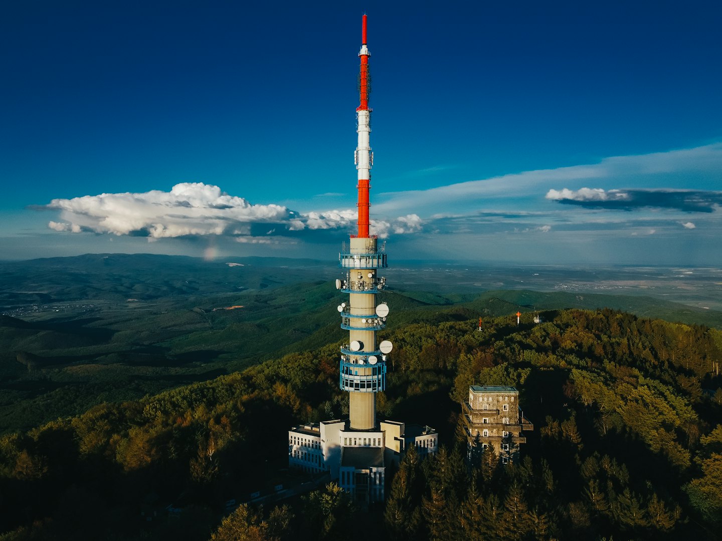 Communication tower and stone building on a forested mountain peak.